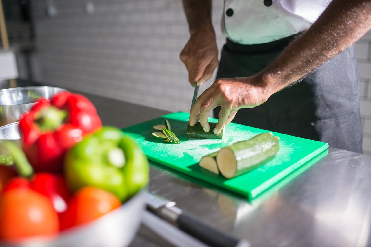 Chef slicing zucchini on a green chopping board with fresh vegetables nearby.